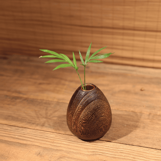 Rin Essense wood vase with natural textured finish holding green leaves on wooden surface