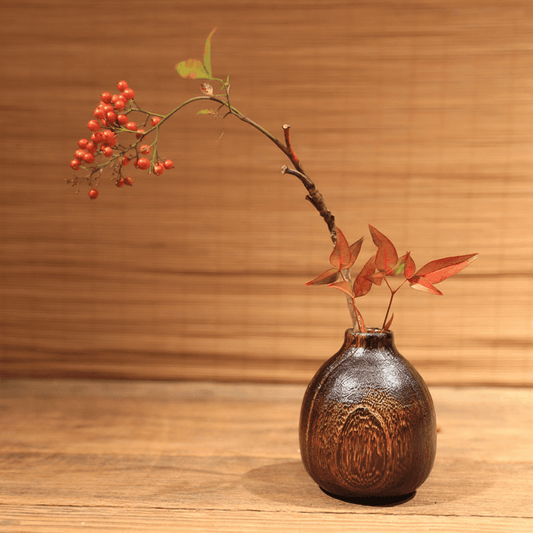 Rin Essense wood vase with rustic dark grain holding autumn leaves and red berries on wooden surface
