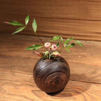 Rin Essense round dark brown wood vase with textured grain holding green leaves and small pink flowers