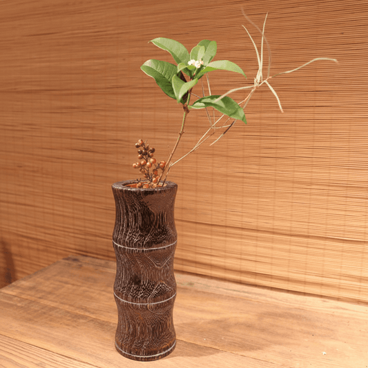 Rin Essense wood vase with carved texture holding decorative green leaves and twigs on wooden surface