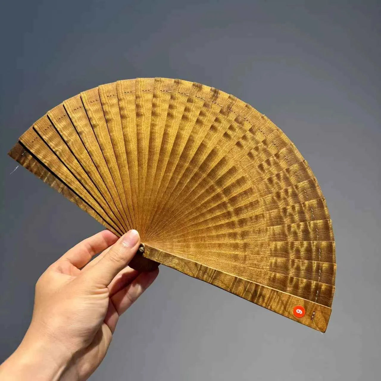 Rin Essense folding fan hand holding brown wooden folding fan with intricate patterns