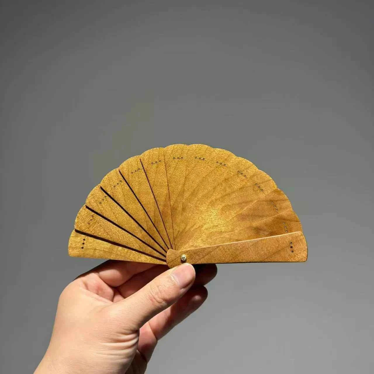 Rin Essense golden folding fan hand held open against a gray background