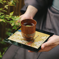Yamanaka Lacquerware Makie Coaster – Timeless Japanese Craft holding a wooden cup with tea on a decorative black tray