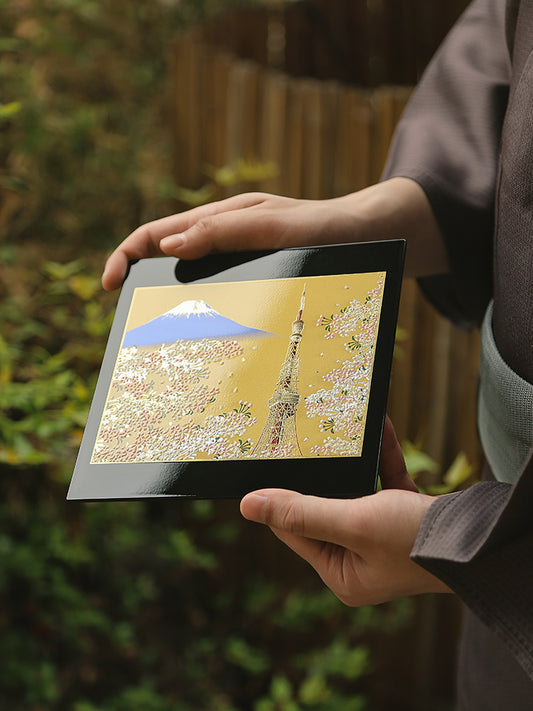 Yamanaka Lacquerware Makie Coaster with Mount Fuji and cherry blossom design held by person in traditional attire