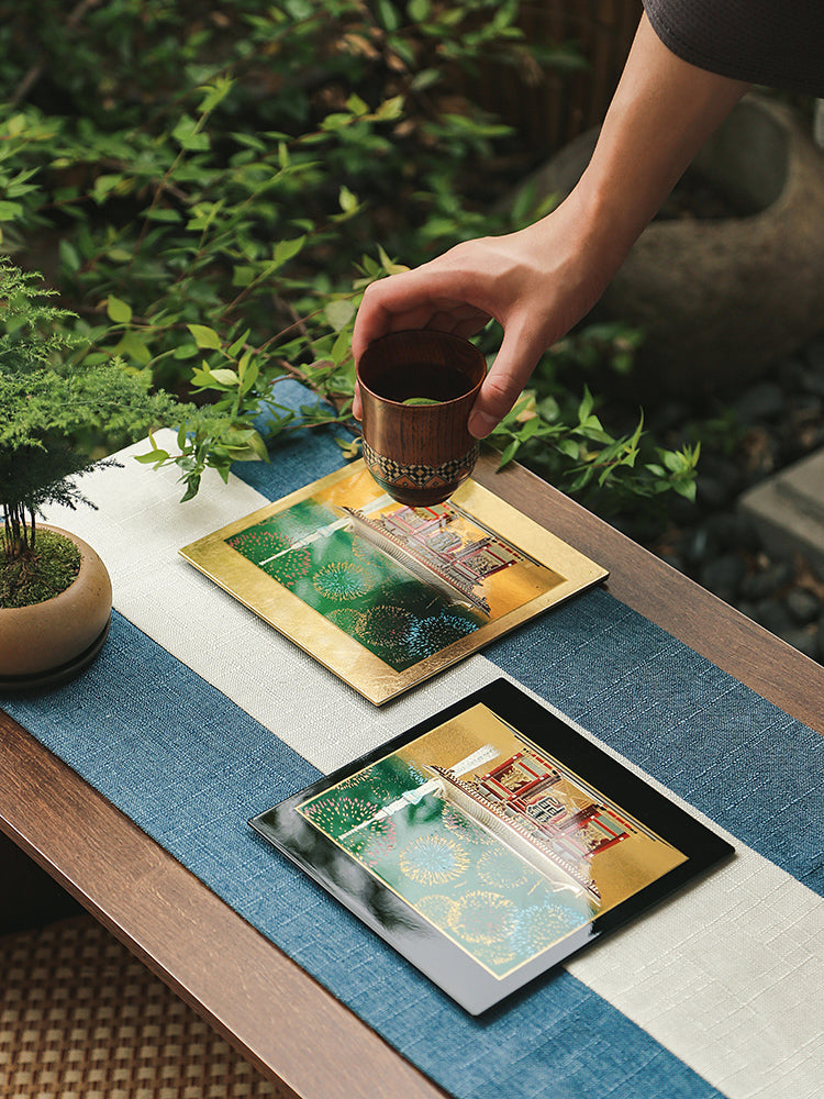 Hand placing a cup on Yamanaka Lacquerware Makie Coaster – Timeless Japanese Craft with intricate gold and green designs on a wooden table