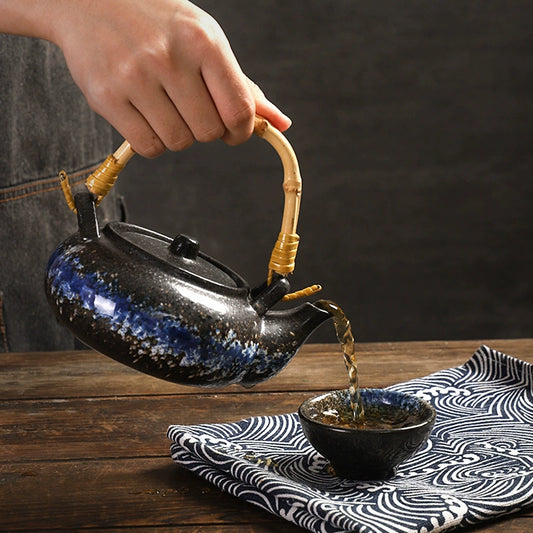 Kokoro ceramic tea set black blue glazed teapot with bamboo handle pouring tea into matching cup on wooden table