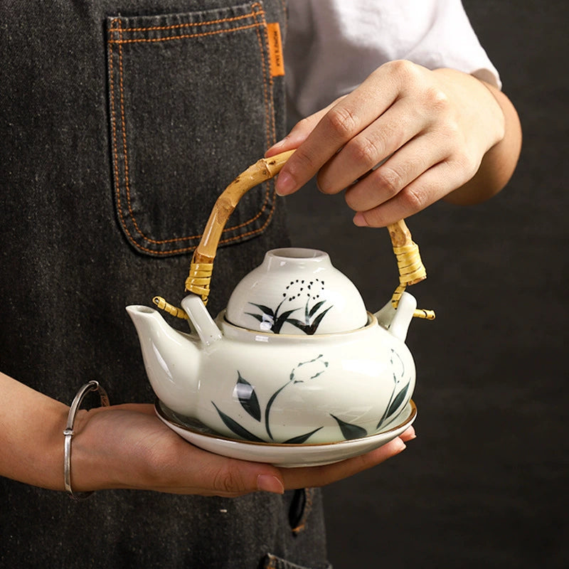 Kokoro ceramic tea set white teapot with bamboo handle and matching cup saucer hand painted green leaf design held by hands